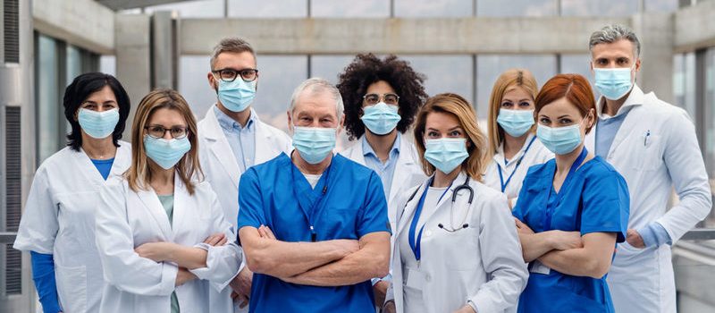 A group of doctors with face masks looking at camera, corona virus concept.