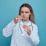 concentrated-young-female-doctor-wearing-medical-robe-stethoscope-around-neck-tapping-syringe-removing-air-bubbles-from-it