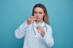 concentrated-young-female-doctor-wearing-medical-robe-stethoscope-around-neck-tapping-syringe-removing-air-bubbles-from-it